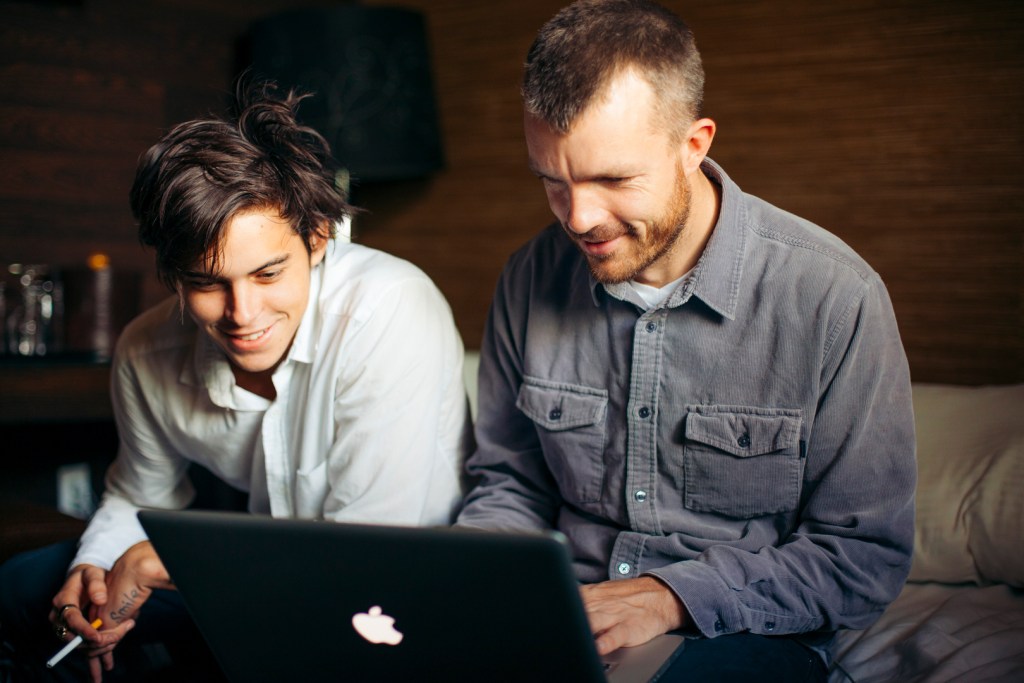 Professional skateboarder Dylan Rieder and cinematographer Greg Hunt look at skateboarding footage on a laptop. The are both smiling, warmly.